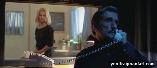 10 Iconic Harry Dean Stanton Performances 11 A man talks on a wired telephone, his back to a well-dressed woman seemingly looking at him through glass.